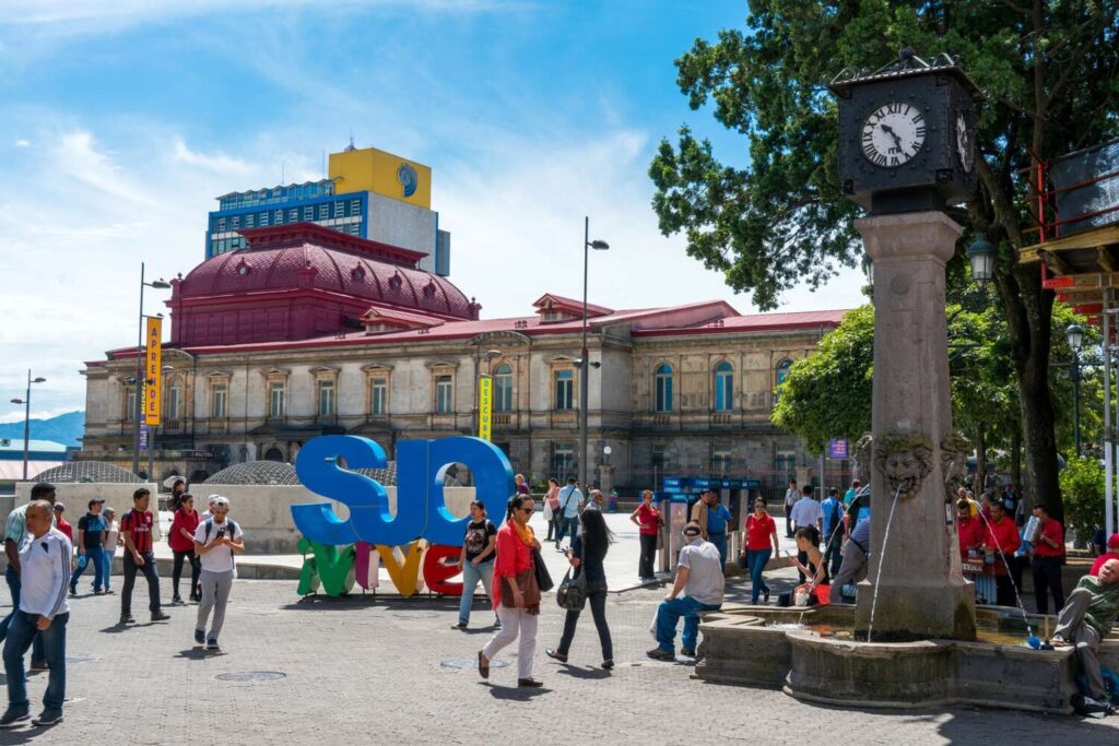 People walking near SJO sign in San José city center.