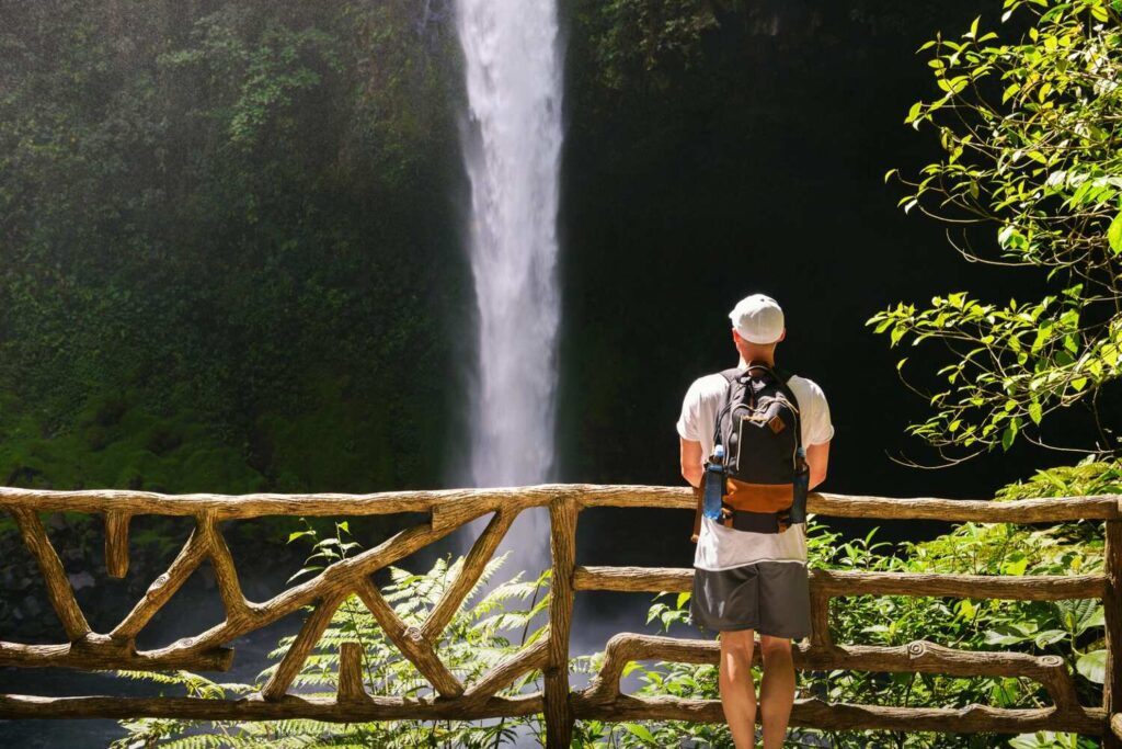 Tourist admiring La Fortuna Waterfall from wooden viewpoint.